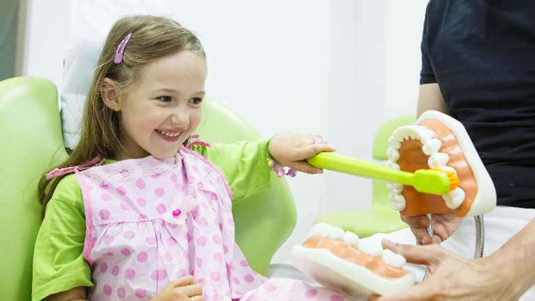 young girl brushing a toy mouth with a large toothbrush to practice brushing technique